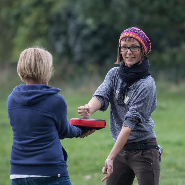 Self-defence trainer Kinga Karp wearing a colourful hat and smiling and practicing punching technique with a trainee outside on a field. 
