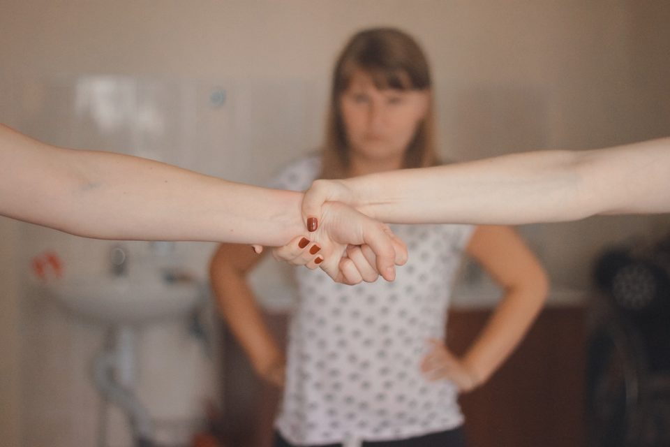 A self-defence trainer in a gym stands in front of two women clasping hands in a training session.