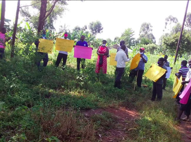 A group of activists from Uganda stand in a circle holding large colourful placards handwritten with slogans.